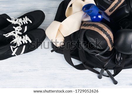 black sports bag with things for training and next to it is wrestling shoes on a light background, close-up
