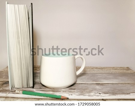 Book, pencil and white mug on a wooden table. White background. Space for your text. Image with selective focus and with toning.