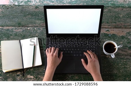POV of women's hands at a rustic table with a laptop, an open notebook with a pencil and a coffee in a cup.