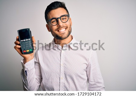Young handsome man doing payment using dataphone over isolated white background with a happy face standing and smiling with a confident smile showing teeth