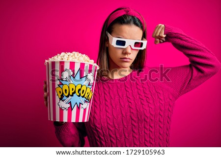 Young beautiful girl watching movie using 3d glasses eating box with popcorns Strong person showing arm muscle, confident and proud of power