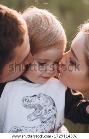 Happy family with son walking in summer field, blowing on dandelion, running, having fun, kissing