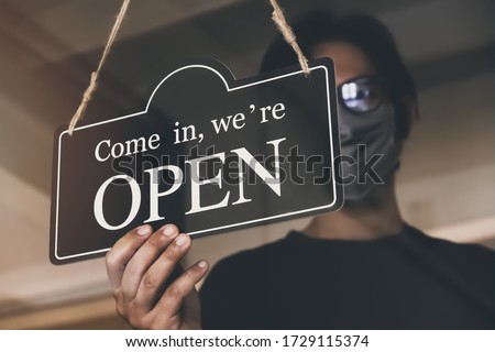 the state allows retail stores or restaurants and businesses to reopen after coronavirus restrictions. man with face mask turning a sign on a door shop. economy starts running after being on lockdown. Royalty-Free Stock Photo #1729115374