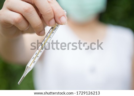 Selective focus of Asian women wear a mask and holding a thermometer on blurred background