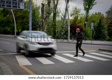 Pedestrian walking on zebra crossing and a driving car failing to stop in blurred motion. Pedestrian reacts with hand to the driver.
 Royalty-Free Stock Photo #1729137013