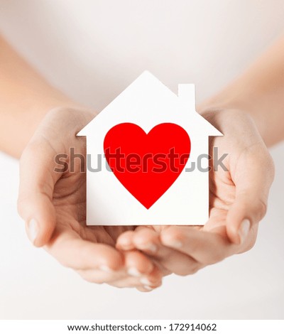 charity, real estate and family home concept - closeup picture of female hands holding white paper house with red heart