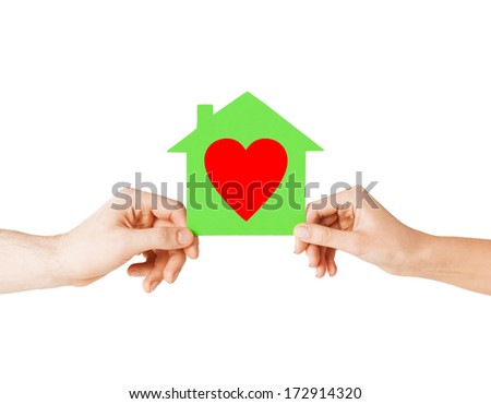 charity, real estate and family home concept - isolated picture of male and female hands holding green paper house with red heart