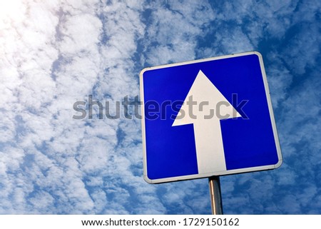 One-way traffic sign against a cloudy sky with sunbeams. Road sign with an arrow on a blue background.