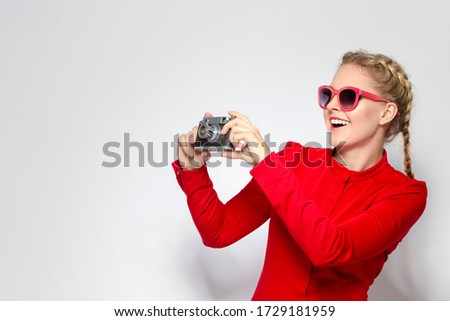 Laughing and Positive Caucasian Blond Girl With Old School Film Camera in Red Dress with Sunglasses. Taking Pictures Against White.Horizontal Image
