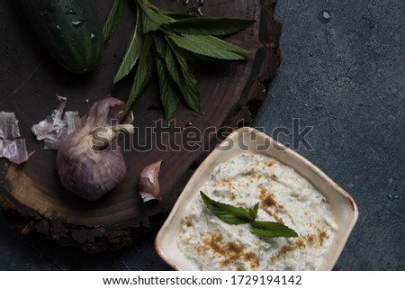Fresh homemade tzatziki sauce with organic garlic, cucumber, and mint on a walnut wood slice and a dark blue background.