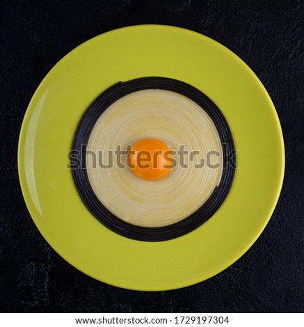 Olive color plate with black and white linguini pasta with egg yolk in the middle over on black background. Minimalistic style. Top view