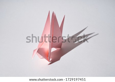 Pink paper dragon figurine stands on a white background in hard light.