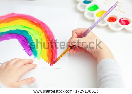 Hand of a small child paints a rainbow by watercolor with a brush.