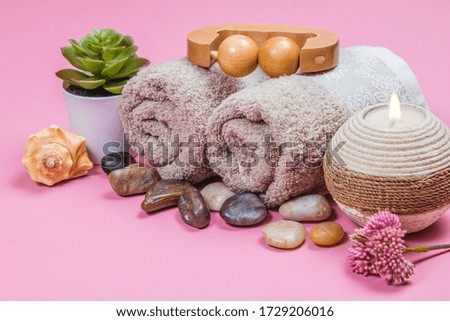 Spa essentials, candle, stones, towel and flowers on a pink background