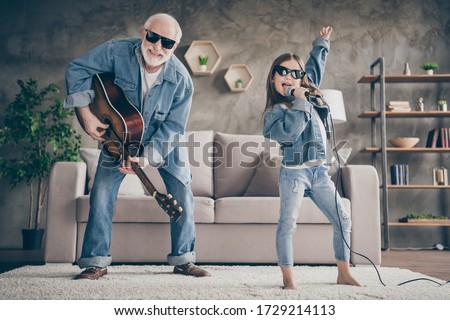 Photo of two people funky grandpa play guitar small nice granddaughter mic singing cool style sun specs denim clothes repetition school concert stay home quarantine living room indoors Royalty-Free Stock Photo #1729214113