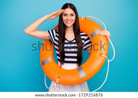Photo of pretty excited lady long hair hold orange emergency life buoy cruise liner trip giving honor boat captain wear white striped summer dress isolated blue background Royalty-Free Stock Photo #1729216876