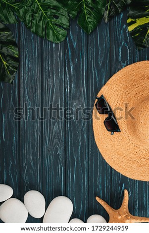 Top view of straw hat and sunglasses near leaves and sea stones on dark wooden background