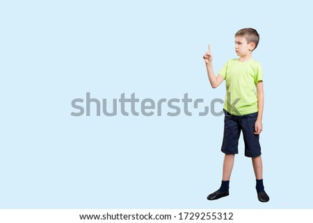 Profile of a young little Caucasian child in a green T-shirt and dark shorts points a finger up. Copyspace
