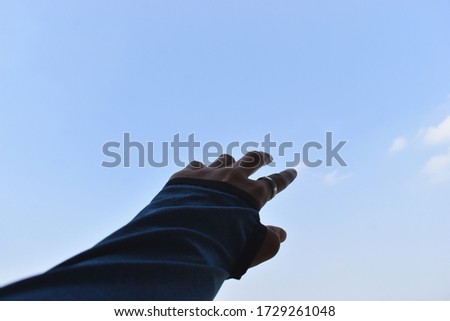 Visible hand with a ring in the index finger pointing towards the white clouds in the blue sky with lots of copy space to add text