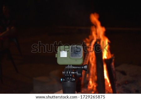A small green colored action camera kept against a bonfire to film it and for video logging 