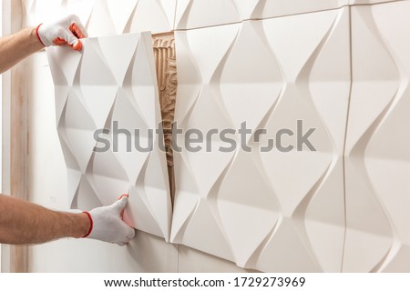 Installation of gypsum 3D panel. A worker is attaching the gypsum tile to the wall. Royalty-Free Stock Photo #1729273969