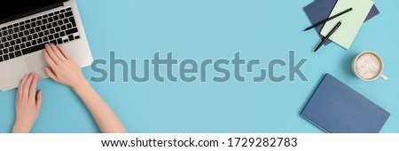 Female hands typing on laptop. Student supplies on a blue pastel background. Banner with copy space. Royalty-Free Stock Photo #1729282783