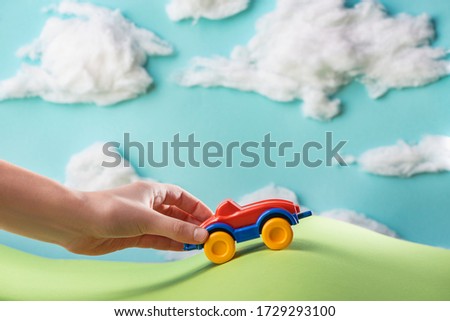 Kid playing with a toy car inside paper world with cotton clouds. Beautiful concept of childhood games.