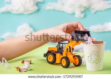 Child playing with a toy truck and loading recyclable garbage into a bin. Paper environment artwork.