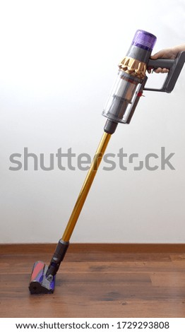 cordless vacuum cleaner on the background of a wooden floor and a white wall