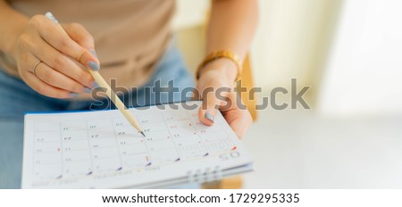 close up on employee woman hand using pen to writing schedule on calendar 2024 to make appointment meeting or manage timetable each day at house for work from home concept	