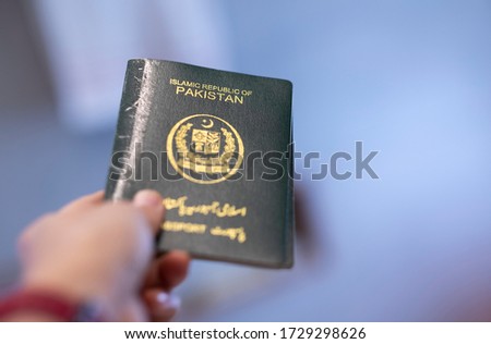 A hand holds passport of Pakistan. Focus on the letters on passport.