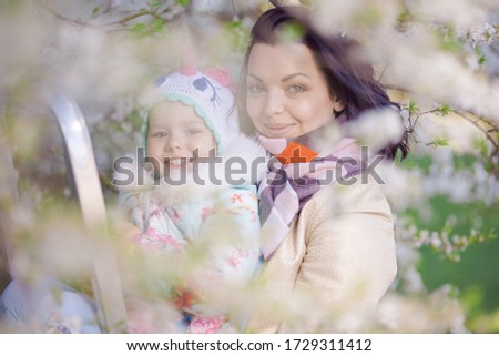 Little girls and young mother play on a stepladder in a blooming cherry garden