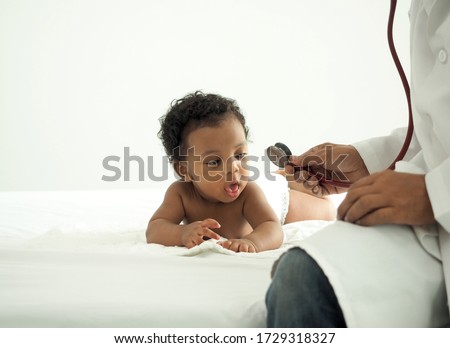 African baby boy is seeing stethoscope in doctor's hand.The child has a surprised expression.