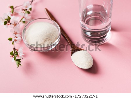 Collagen powder in wooden spoon, supplement with galss of water and flowers, healthy and anti age concept  on pink background, top view, copy space Royalty-Free Stock Photo #1729322191