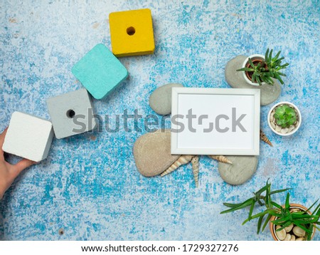Top view of picture frame mockup with succulent plants, rocks, sea shelves and summer decorations on old blue table.