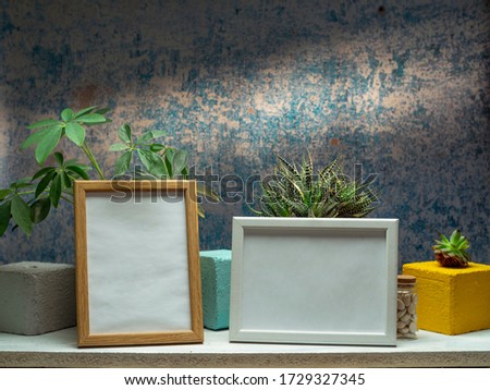 Two picture frame mockups and plants on white shelf against old blue wall.
