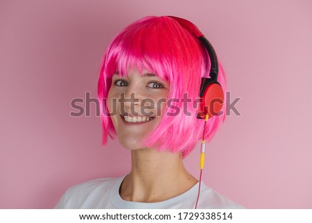 beautiful happy young woman with pink hair using red headphones and listening music on a pink background

