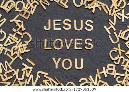 wooden letters JESUS LOVES YOU on slate background
