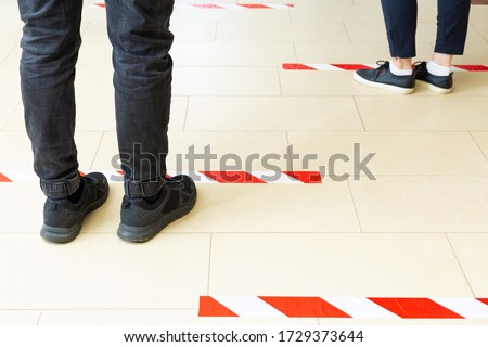 People stand in line keeping social distance, standing behind a warning line during covid 19 coronavirus quarantine. Safe shopping, Social distancing concept. Legs in line close up Royalty-Free Stock Photo #1729373644