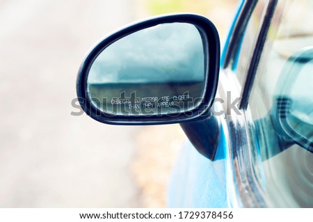 The inscription on the car side mirror: "Objects in mirror are closer than they appear", closeup. A concept of warning, safety and care for the driver. Car's Reflection In Rear View Mirror. 