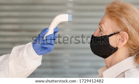 caucasian senior woman standing for temperature scanning with digital device for fever check in coronavirus covid-19 spreading prevention and protection method Royalty-Free Stock Photo #1729412482