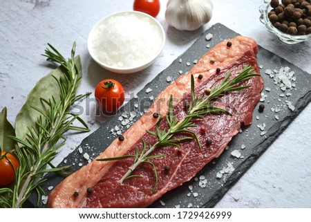 Raw meat with rosemary, spices and tomatoes on a black slate on a light background.