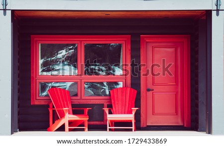 Two empty red patio chairs on the deck of a porch with a red door