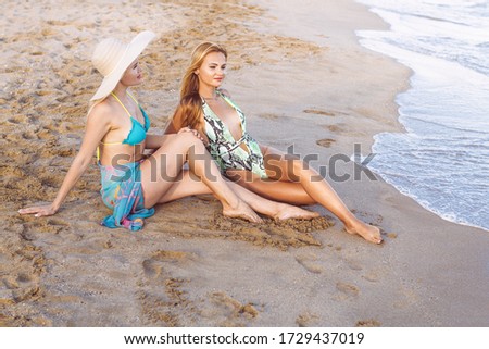 couple of two blonde girls sitting on the shore looking the sea, concept of friendship and relaxation in the summer