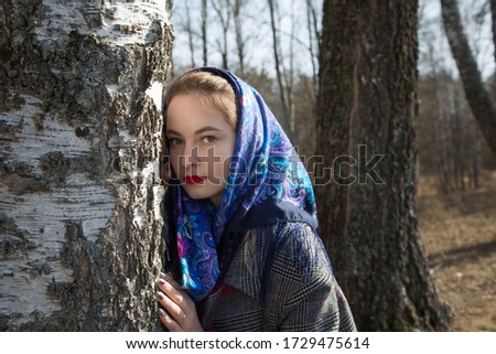 Russian beauty in a scarf near a birch.Image with selective focus, toning and noise effect.