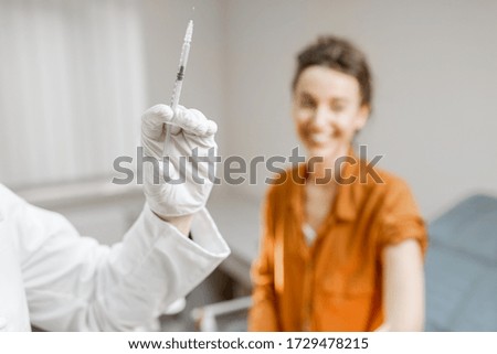 Doctor holding vaccine or some medication in the syringe, preparing for injection for a young woman during a medical procedure in the clinic