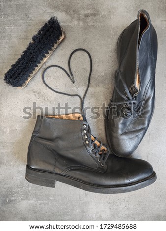 Pair of black leather retro shoes and wooden shoe brush on grey background with copy space. 
