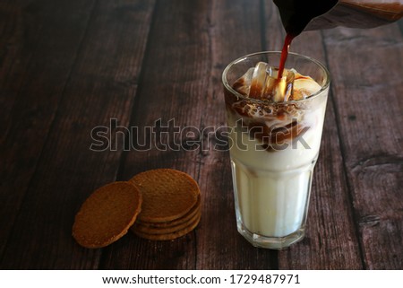 A glass of iced milk poured espresso shot  have biscuits beside. Iced coffee with cookies on wooden table.