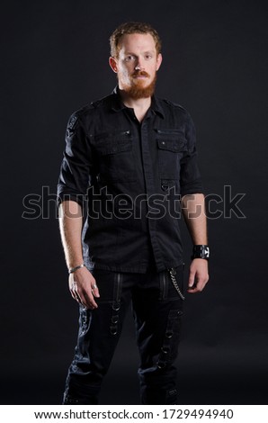 Portrait of a redhead man posing on black background with goth metal style clothing.