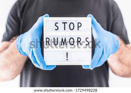 Fake news infodemics during Covid-19 pandemic concept. Man wearing protective mask and medical gloves on hands holding lightbox with text Stop rumors. People want to know the truth about coronavirus